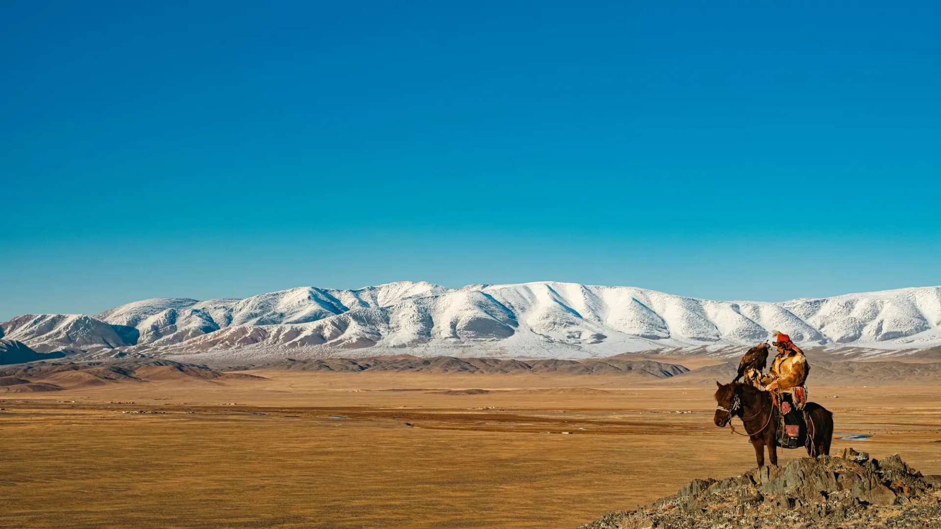 Autumn steppe below snowy mountains, a rider in the distance